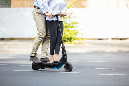 Portrait Of Happy Couple Riding On Electric Scooter Over The Street In The City
