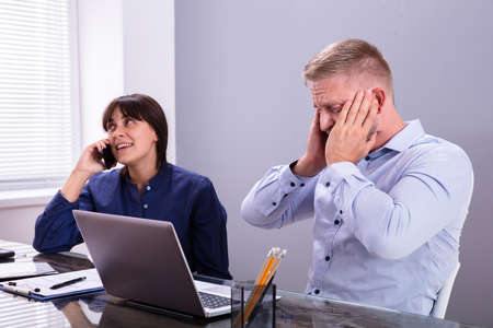 Businessman Irritated With Female Colleague Taking On Mobile Phone At Work In Office