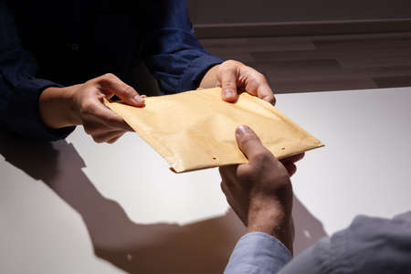 An Elevated View Of Man Receiving Brown Bribe Packet From Woman Over The White Deskの写真素材