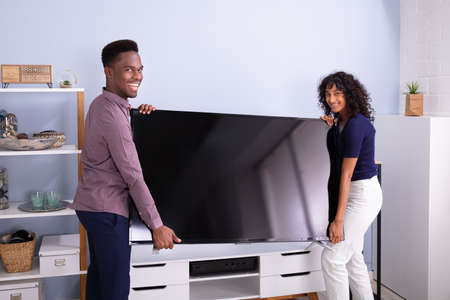 Side View Of Young Couple Lifting Television At Homeの写真素材
