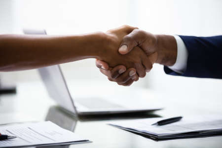 Two Businesspeople Shaking Hands At Desk In Officeの写真素材