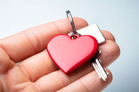 Close-up Of A Person's Hand Holding Red Heart Shape Key Chain With Keyの写真素材