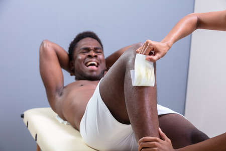 Man Screaming In Pain While Waxing Leg With Wax Stripの写真素材
