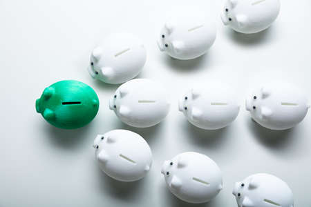 White Piggybanks Following Green Piggybank On White Backgroundの写真素材