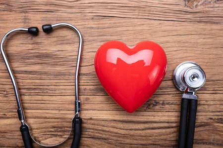 High Angle View Of Stethoscope Arranged Near Red Heart Against Wooden Tableの写真素材