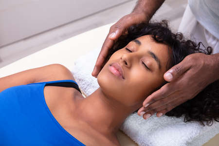 Close-up Of Therapist's Hand Performing Reiki Treatment On Young Woman In Spaの写真素材