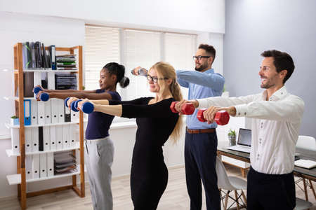 Happy Young Businesspeople Standing In Row Exercising With Dumbbells In Officeの写真素材