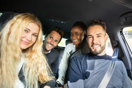 Close Up Of Smiling Multi Racial Friends Sitting Inside Car Looking At Cameraの写真素材