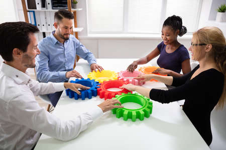 Group Of Businesspeople Arranging Colorful Cog Wheels Together Over White Table At Officeの写真素材