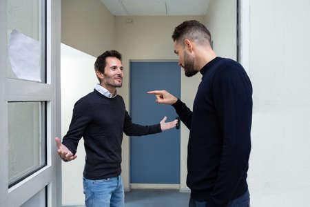 Two Young Men Standing At The Door Entrance Quarreling With Each Other