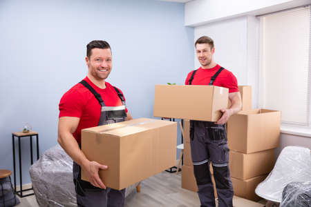Portrait Of Two Smiling Young Male Relocation Worker Carrying Cardboard Boxes In The Living Roomの写真素材