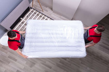 Two Male Professional Movers In Uniform Placing The Mattress Over The Bed In New Houseの写真素材