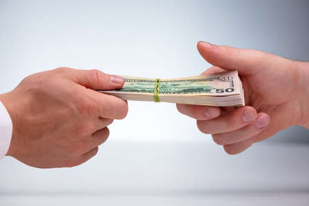Close-up Of Two Male Hand's Holding Currency Bundle Tied With Elastic Rubber Against Gray Background