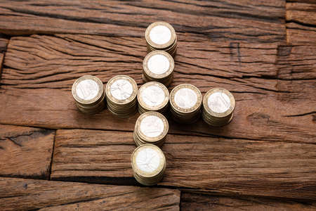 Stacked Coins Forming Plus Sign On Wooden Desk