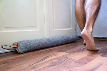 Person Walking Barefoot Near Draft Excluder Under Door Blocking Cold Air From Traveling Aroundの写真素材