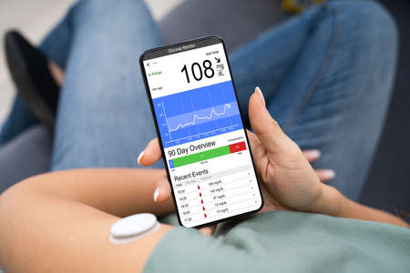 Woman Holding Smartphone In Hand With Bad Level Of Blood Sugar On The Screenの写真素材