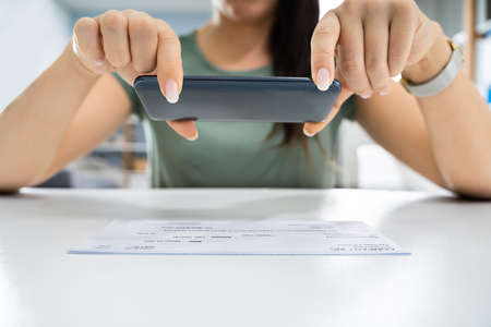 Woman Taking Photo Of Cheque To Make Remote Deposit In Bankの写真素材