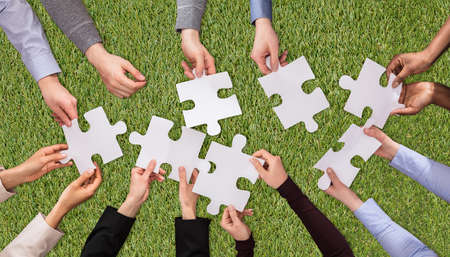 An Overhead View Of People Hands Joining The White Jigsaw Puzzles On Green Grass Turfの写真素材