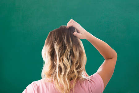 Rear View Of Blonde Young Woman Scratching Her Head Against Green Backgroundの写真素材