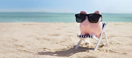 Pink Piggybank Wearing Eyeglasses On Deck Chair Over The Sandy Beachの写真素材