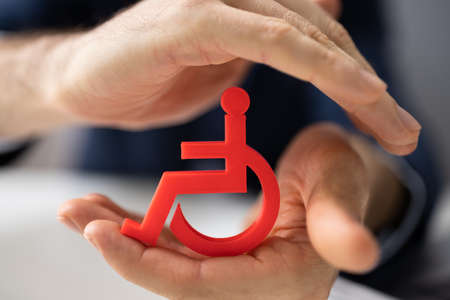 Close-up Of A Person's Hand Protecting Blue Cubic Block With Disabled Iconの写真素材