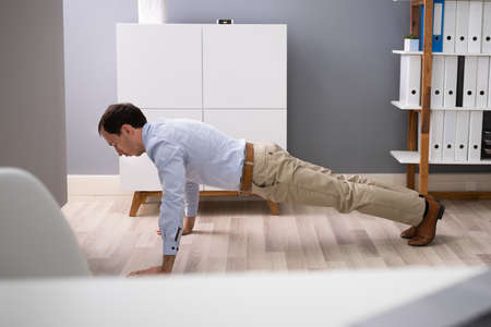 Side View Of A Young Businessman Doing Push Up In Office