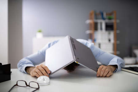 Businessman Hiding His Face With Laptop In Office
