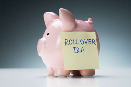 Close-up Of Rollover Ira Text On Sticky Note With Pink Piggy Bank Over White Desk