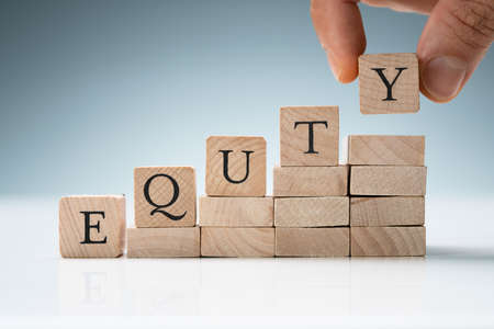 Human Hand Arranging Stack Of Wooden Blocks In A Row Showing Equity Textの写真素材