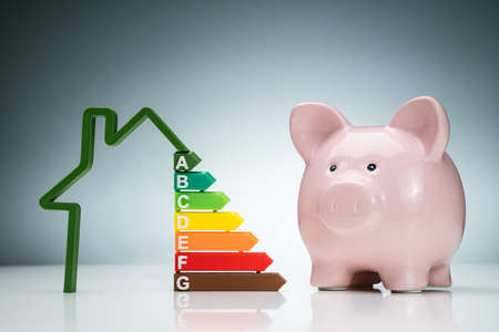 Green House Energy Efficiency Graph Near The Pink Piggybank On White Desk Against Blue Background
