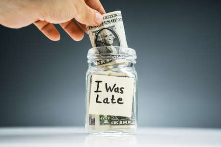 Man's Hand Putting The Us Dollar Notes To The Glass Jar With Adhesive Notes
