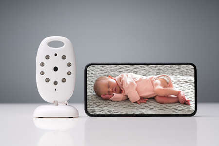 Close-up Of Wireless Camera And Smartphone With Baby Image On Screen On Reflective Tableの写真素材