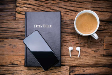 High Angle View Of Bible And A Smart Phone With Wireless Earphones And Empty Teacupの写真素材