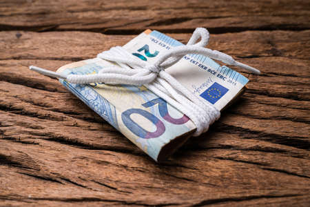 Bundle Of Euro Currency Banknotes Tied With White Lace Over Rough Wooden Textured Backdropの写真素材