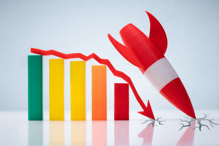 Red Rocket Landing Near Declining Graph With Downward Directional Arrow Over Reflective Deskの写真素材