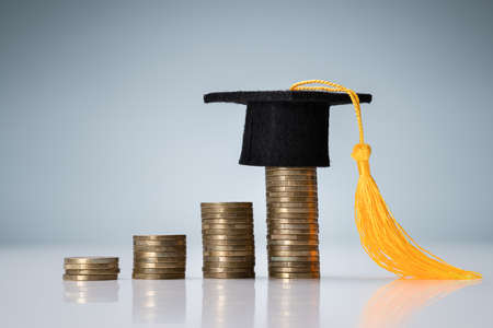 Miniature Of Graduation Hat On Top Of Increasing Coin Stack Over Reflective Deskの写真素材