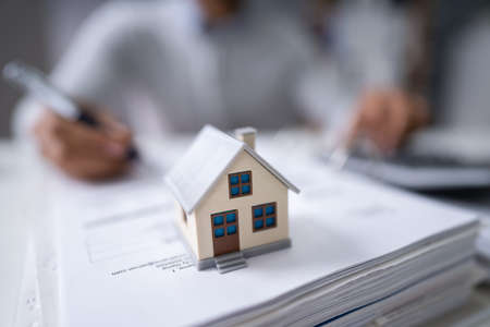 Businessman's Hand Calculating Invoice With House Model In Officeの写真素材
