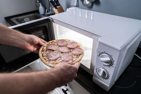Human Hand Baking Pizza In Microwave Ovenの写真素材