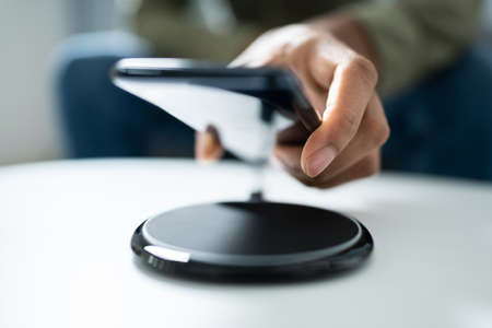 Man Charging Smartphone Using Wireless Charging Pad At Home