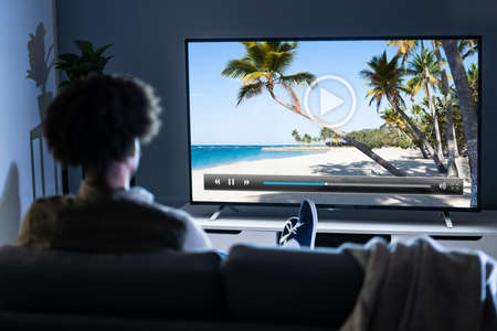 African Man Sitting On Sofa With Remote Holding In Hand