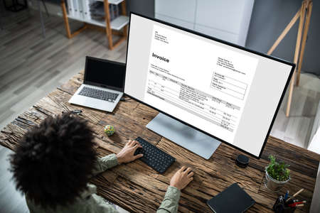 Close-up Of A Businessperson's Hand Analyzing Invoice On Laptop At Workplaceの写真素材