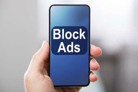 Person's Hand Holding Mobile Phone With Screen Showing Block Ads Message Against Blur Backgroundの写真素材