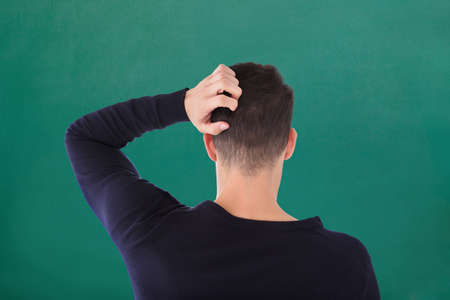 Rear View Of Young Man In Blue T-shirt Scratching His Head Against Green Backgroundの写真素材