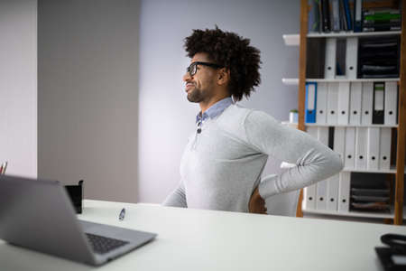 Young Businessman With Backpain Sitting On Chair At Workplaceの写真素材