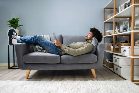 Man Using Digital Tablet Lying In Sofa