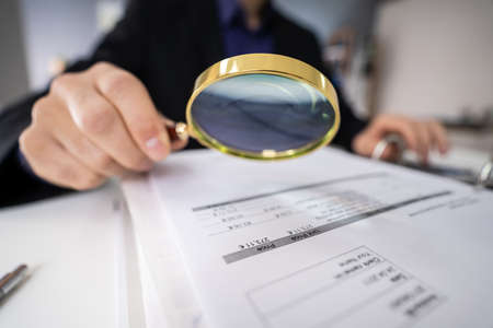 Close-up Of Businessperson Checking Bills With Magnifying Glassの写真素材