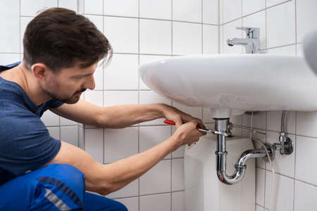Young Plumber Fixing A Sink In Bathroomの写真素材