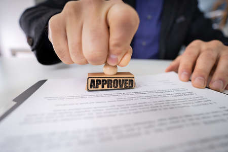 Close-up Of Person Hands Using Stamper On Document With The Text Approvedの写真素材