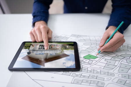 Hand Holding Pencil Over Cadastre Map New Tablet With House Imageの写真素材