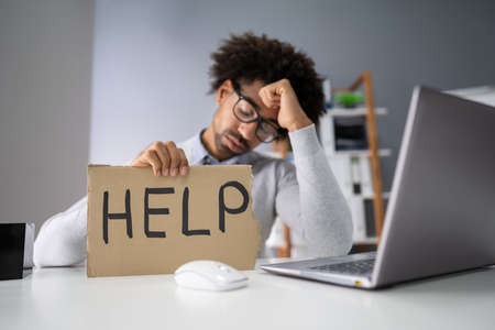 Stressed Young Businessman Holding Cardboard With Help Text In Officeの写真素材